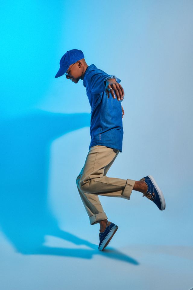 Model in blue cap and denim mid-step against blue light